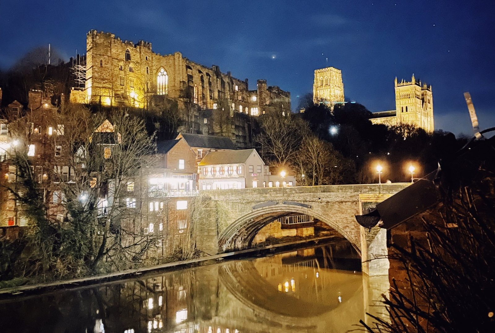 Durham Castle and Cathedral lit up above the River Wear at dusk